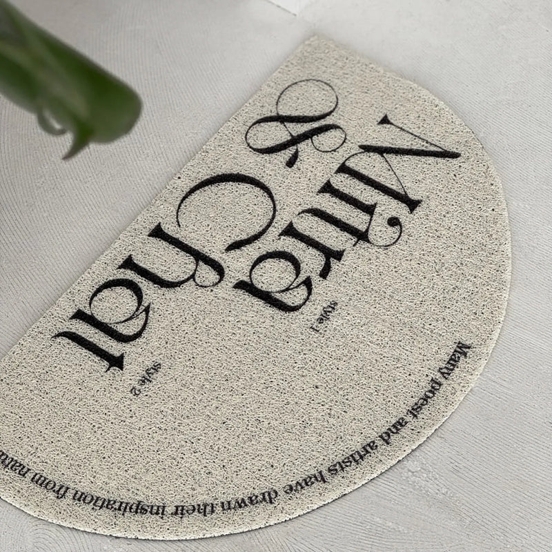Top-down view of a cream semi-circle PVC coil rug with black vintage typography - RoomDen