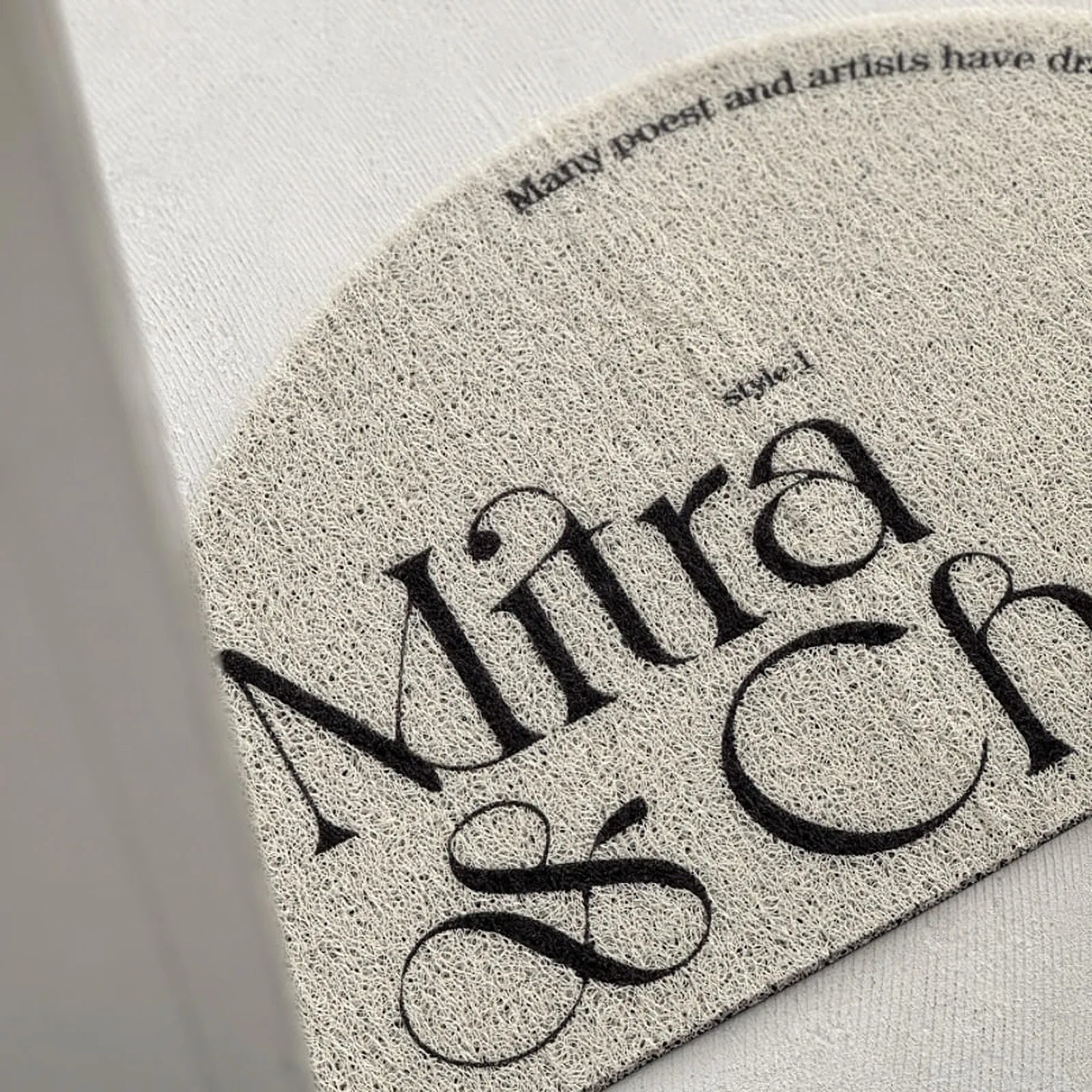 Angled close-up of the "Mira & Chat" typography on the cream half-moon entrance mat.