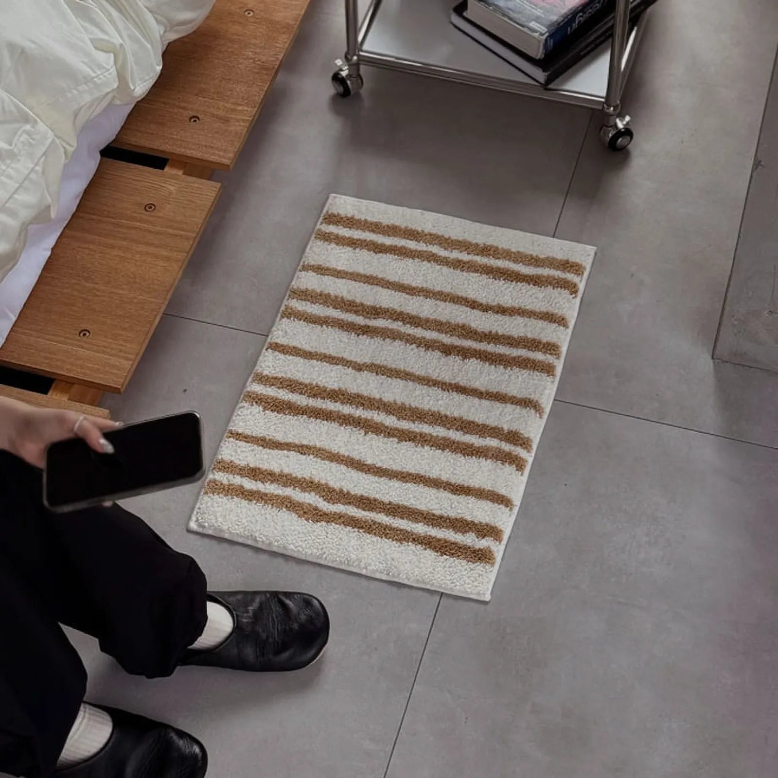 Lifestyle shot of person sitting next to the toast-colored striped rug holding a phone - RoomDen