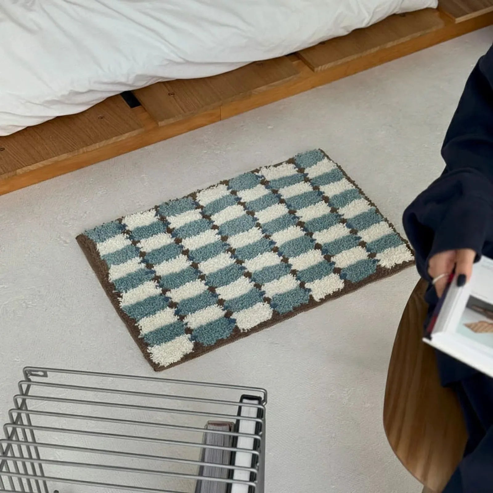 High angle view of Wavy Checkerboard Plush Accent Rug on concrete floor next to a wire rack and person reading - RoomDen