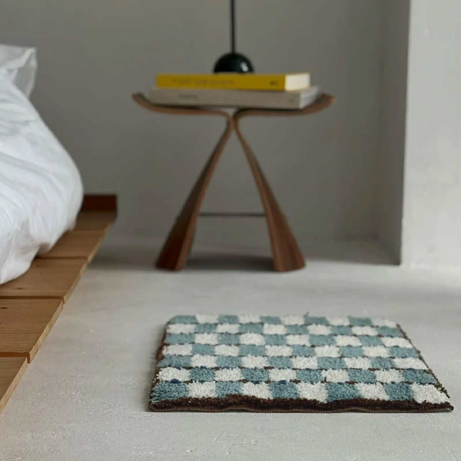 Wavy Checkerboard Plush Accent Rug placed beside a wooden platform bed and sculptural stool in a minimalist bedroom - RoomDen