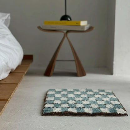 Wavy Checkerboard Plush Accent Rug placed beside a wooden platform bed and sculptural stool in a minimalist bedroom - RoomDen