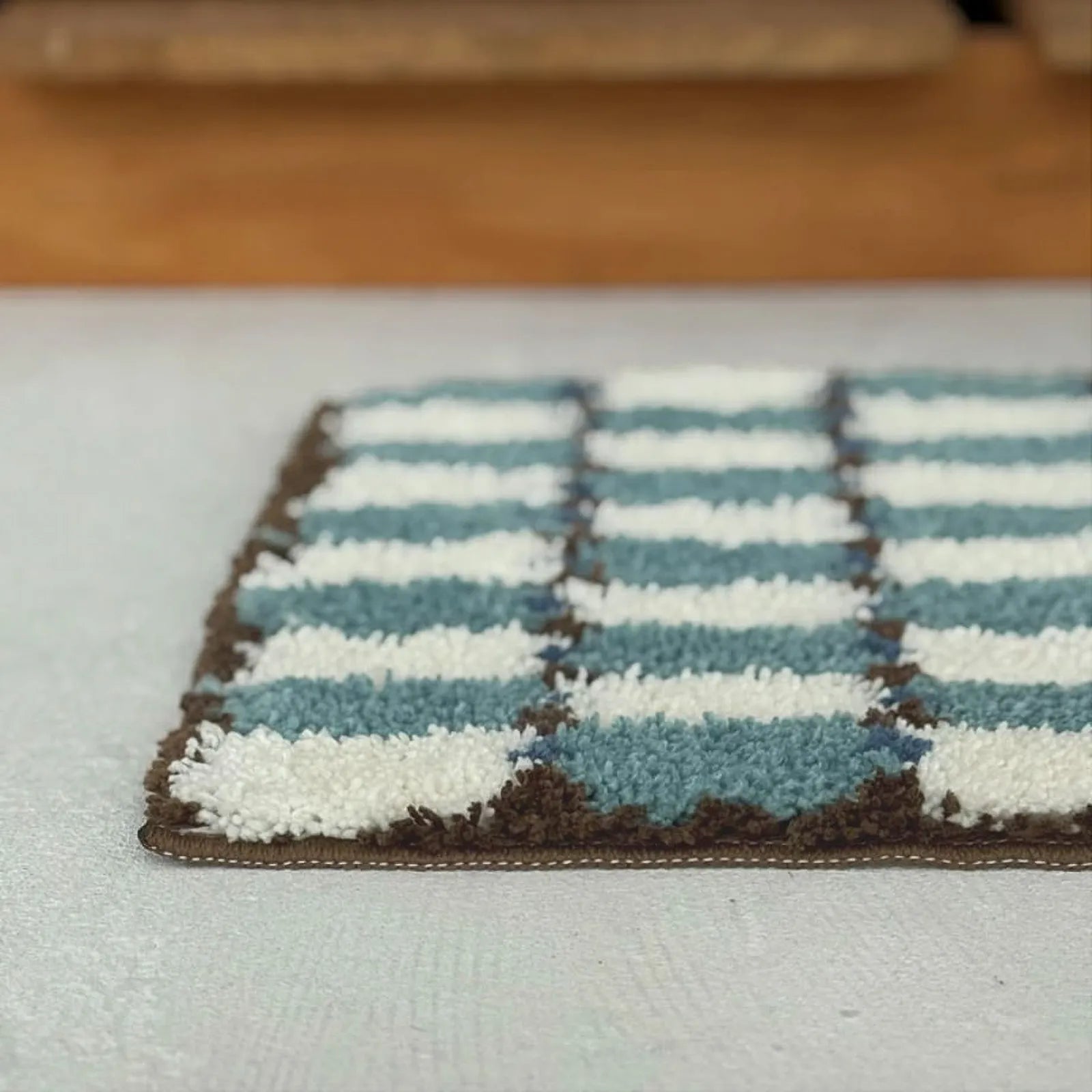 Extreme close-up detail of Wavy Checkerboard Plush Accent Rug showing dense flocked texture and brown stitched edging - RoomDen