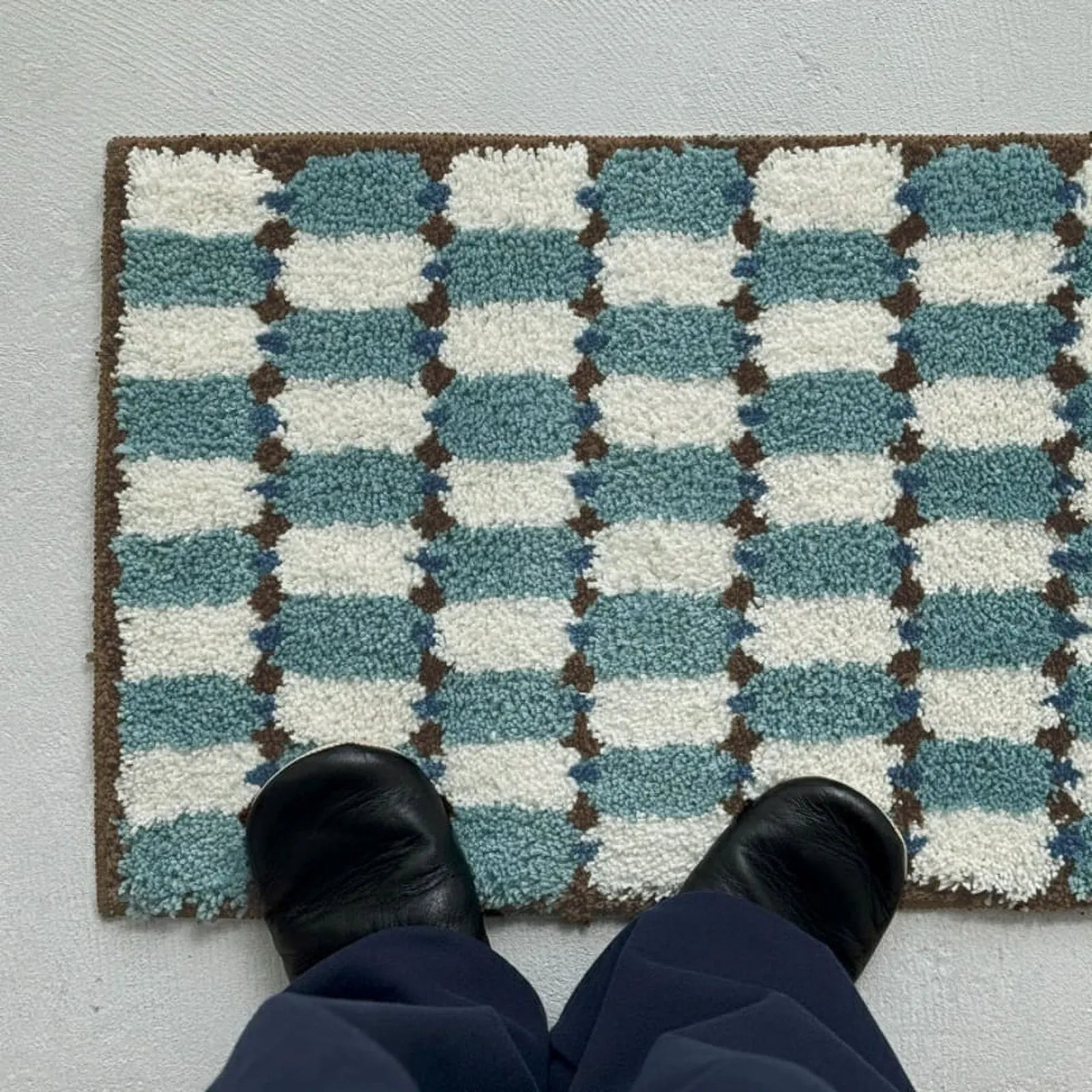 Top-down view of feet in black leather shoes standing on Wavy Checkerboard Plush Accent Rug highlighting the geometric pattern - RoomDen