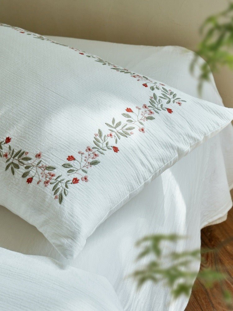 Embroidered ivory bedding in a softly lit bedroom - Roomden
